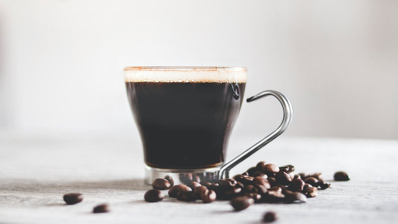 Cup of black instant coffee with roasted coffee beans on a white table