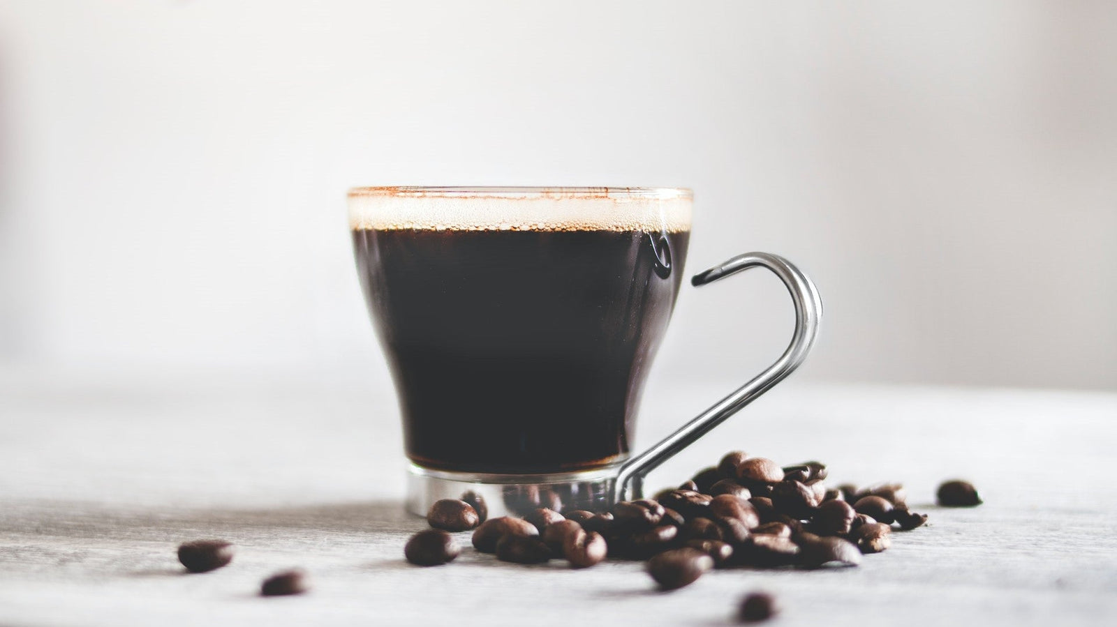 Cup of black instant coffee with roasted coffee beans on a white table